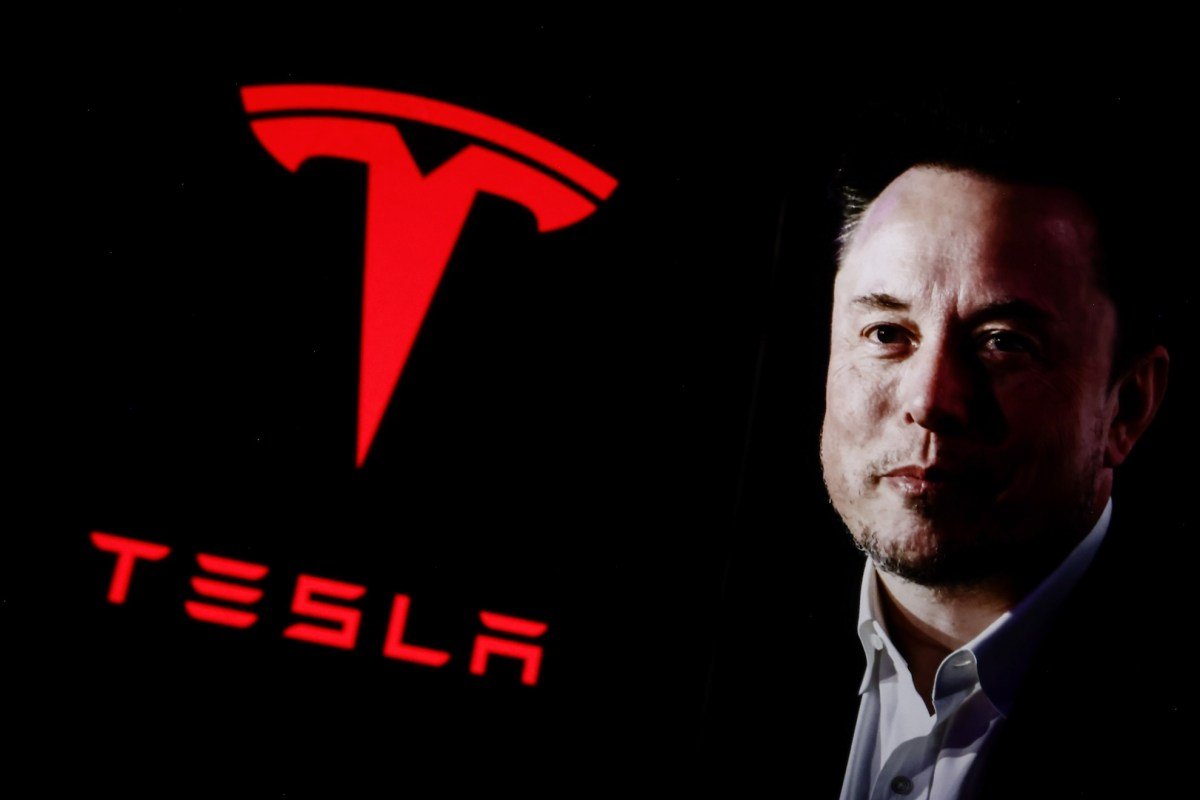 Elon Musk next to large red Tesla logo