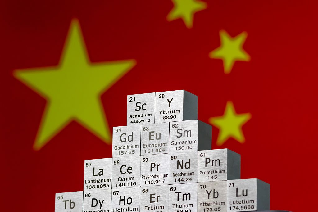 In this photo illustration, metal cubes representing rare earth elements including Scandium (Sc), Yttrium (Y), Neodymium (Nd), Lanthanum (La), and others are stacked in a stepped formation in front of the national flag of China