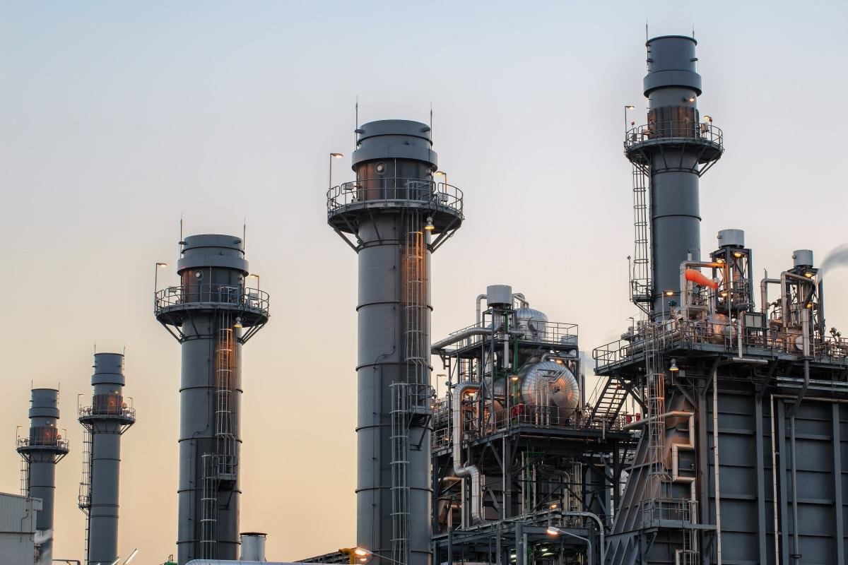 Natural gas power plant smoke stacks stand against a twilight sky.