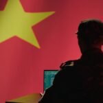 A man sits in front of a computer and the Chinese flag.