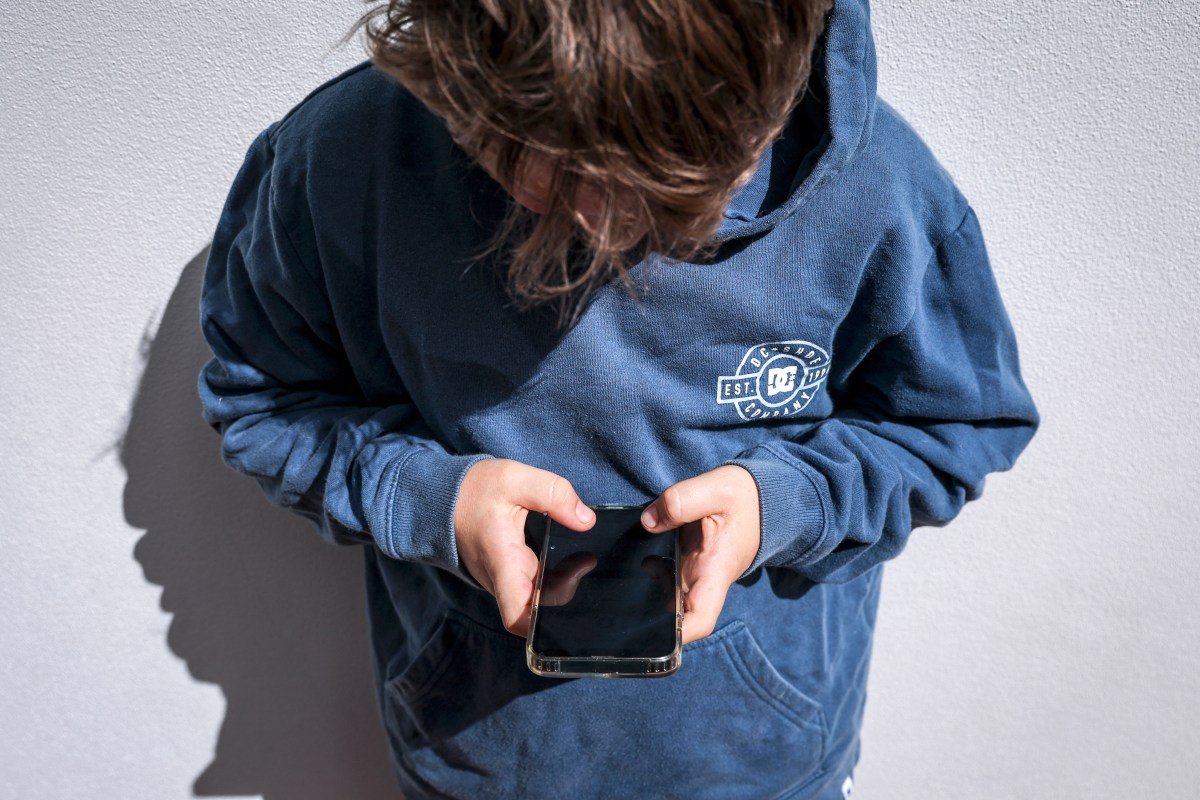 Shows a 14-year-old boy as he looks at social media on his mobile phone.