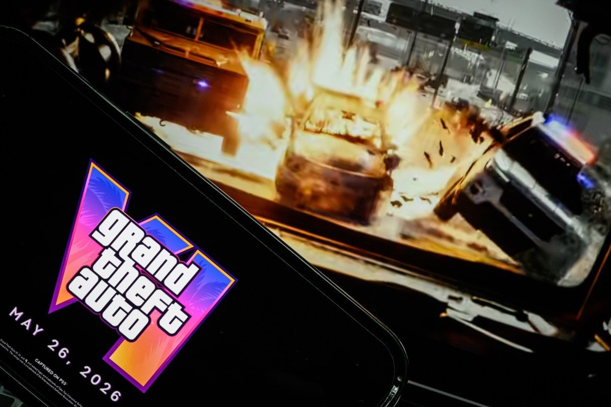 LONDON, ENGLAND - MAY 06: In this photo illustration, a phone displaying the Grant Theft Auto VI logo and new release date is shown in front of a screen displaying the second official trailer for the game, on May 06, 2025 in London, England. Last week, Rockstar Games, developer of the Grand Theft Auto franchise, announced the game had been pushed back to May of next year.