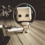 Wooden Robot Android Stands On A Table Under A Magnifying Glass. Metal Clamps With Magnifying Glass