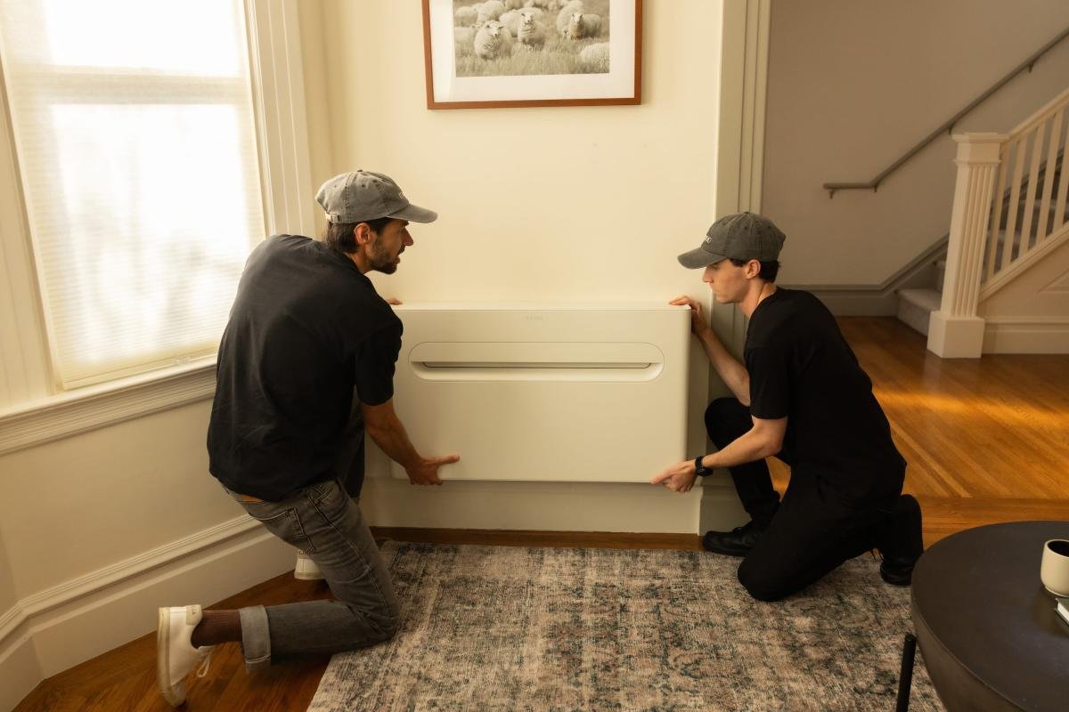 Two men install a heat pump on a wall.