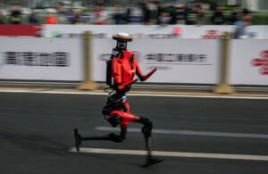 The fastest humanoid robot, an H1made by Honor, runs beside human runners at the start on its way to winning the Beijing Humanoid Half Marathon.
