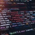 Close-up of computer screen showing colorful programming code lines with syntax highlighting and blurred light reflections.