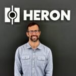 Drew Baglino standing in front of the Heron Power logo.