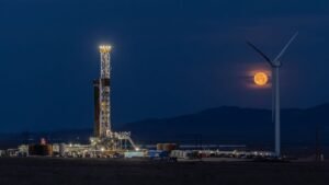 Fervo's drilling rig lit up at night with the moon rising in the background.