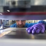 A man reaches his hand into a machine to grab a battery prototype.